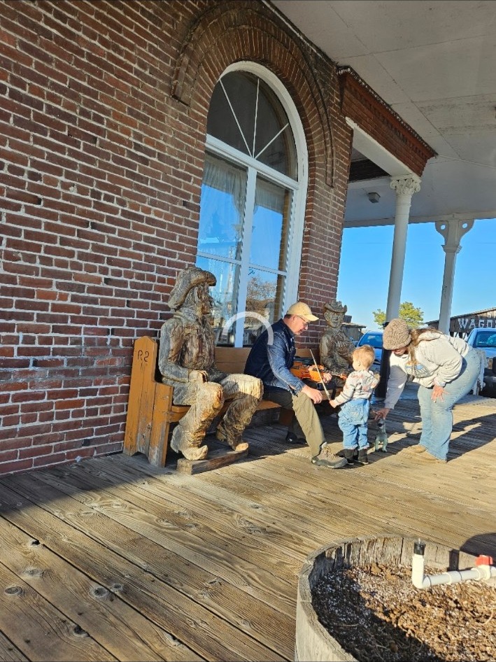 Visitors enjoying the wooden porch and carved figures in historic Shaniko